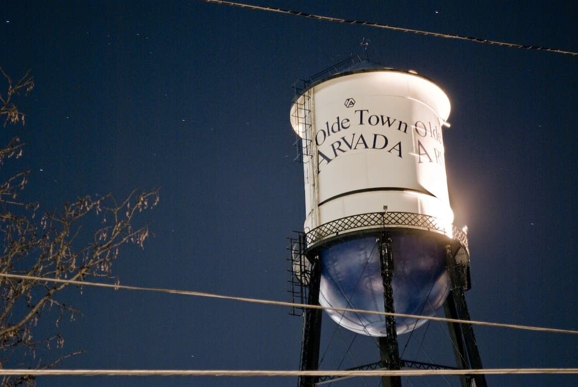 The illuminated Olde Town Arvada water tower at dusk, its 'Olde Town Arvada' lettering glowing against a deep blue sky