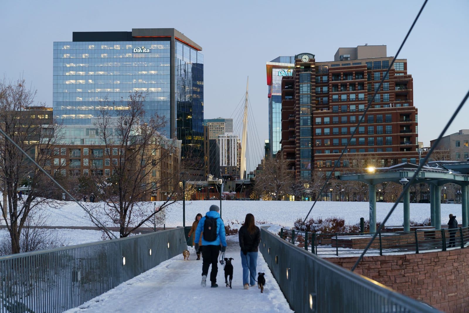 The Highland pedestrian bridge over I-25 at twilight, leading toward the lit downtown Denver skyline