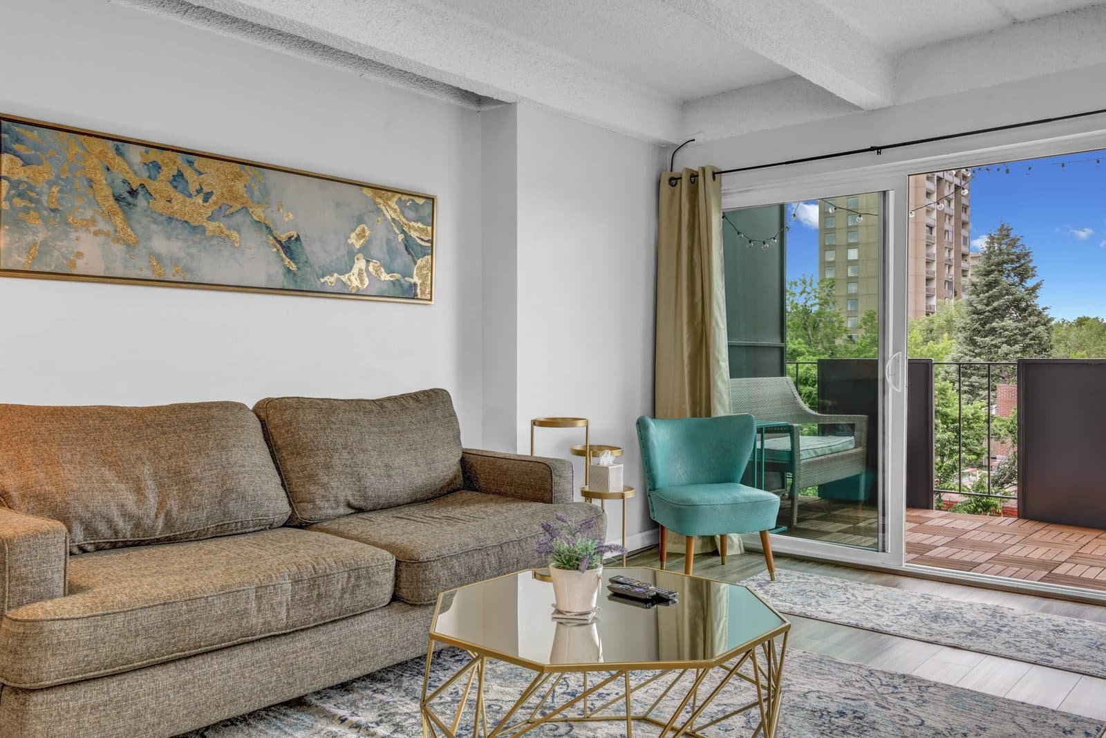 Living room with sofa, teal velvet accent chair and an open balcony door with park view